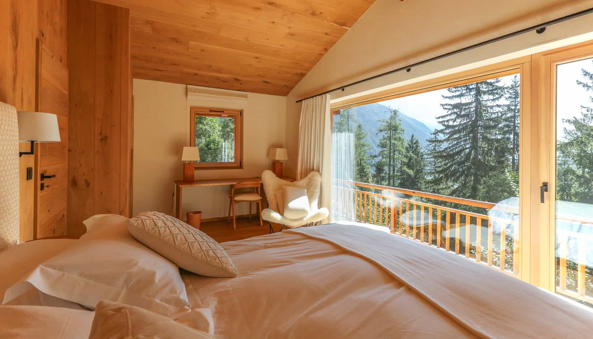 Chambre lumineuse avec grande fenêtre offrant une vue imprenable sur la forêt et les montagnes.